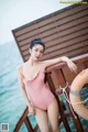 A woman in a pink bathing suit leaning on a wooden railing.