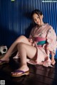 A woman in a pink kimono sitting on a wooden floor.