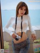 A woman in a white shirt and jeans holding a camera.